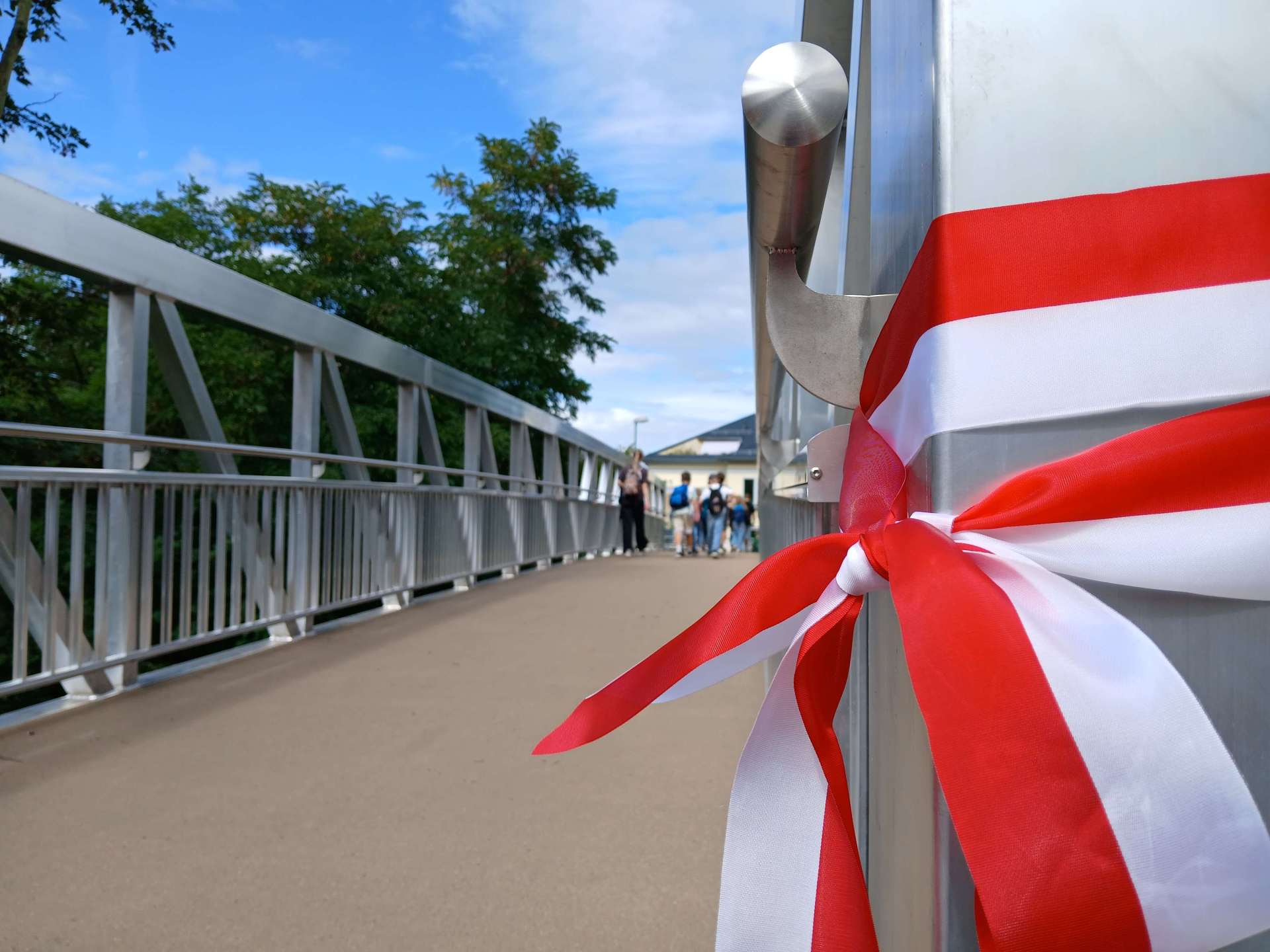 Durchgeschnittenes Band nach Eröffnung einer Brücke; im Hintergrund Schüler, die die Brücke überqueren