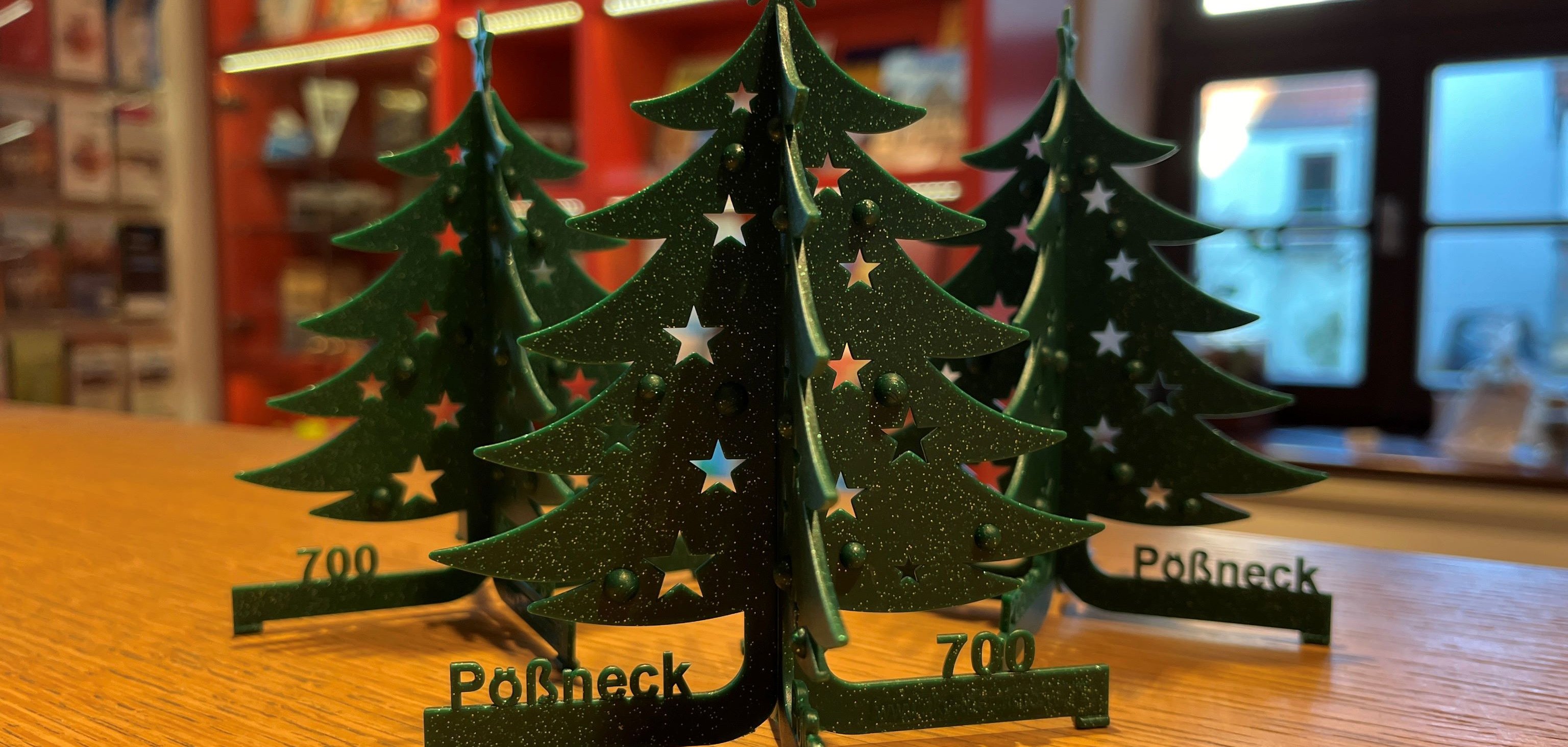Nahaufnahme von drei Weihnachtsbäumen aus Kunststoff mit dem Schriftzug "Pößneck 700"