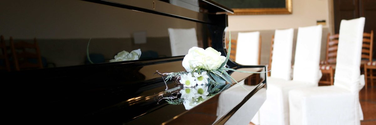 geschlossenes Klavier mit Blumen, im Hintergrund vier Stühle mit Stuhlhussen für Eheschließung