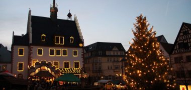Adventsmarkt der Vereine Blick auf abendlichen Weihnachtsmarkt mit stimmungsvoll beleuchtetem Rathaus und Weihnachtsbaum